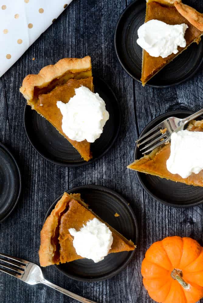 aerial view of 4 plates with pumpkin pie with whipped cream against black background. 