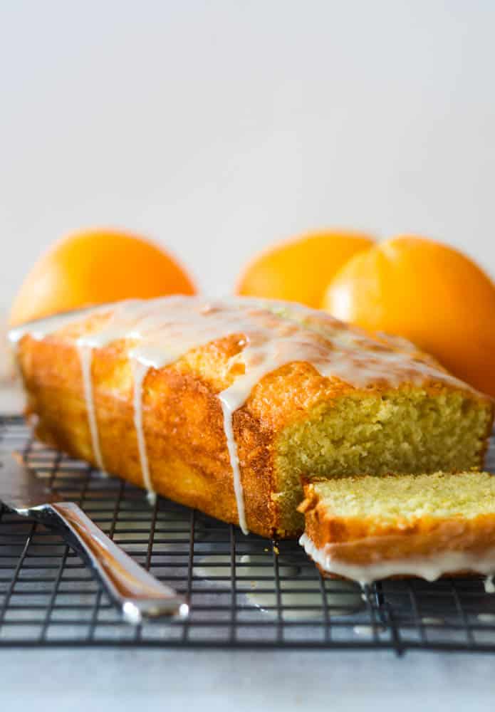 side view of pound cake with orange glaze drizzled on top and oranges in the background. 