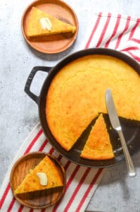aerial picture of cornbread in cast iron skillet with two pieces cut out.