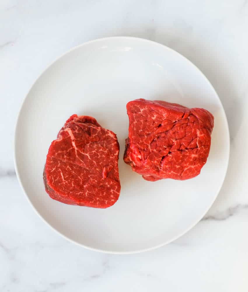 aerial picture of raw beef tenderloin on white plate against marble background.