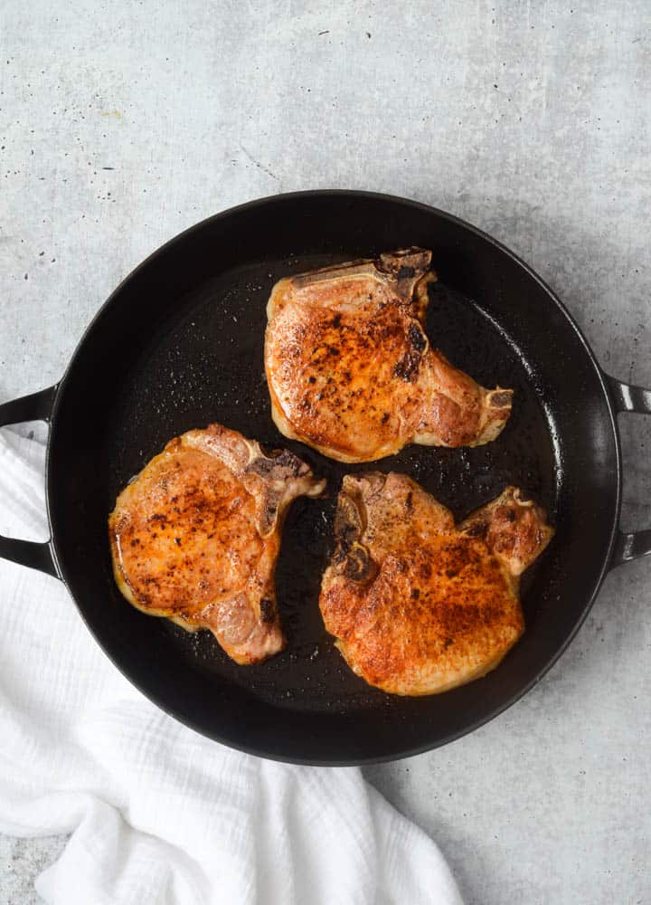 aerial picture of 3 cooked pork chops in a cast iron skillet. 
