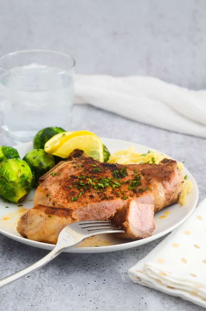 close up picture of pork chop with a bite of meat on a fork. 