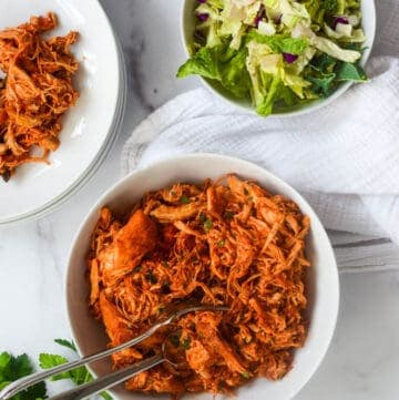 large white bowl of shredded chicken against marble backdrop.