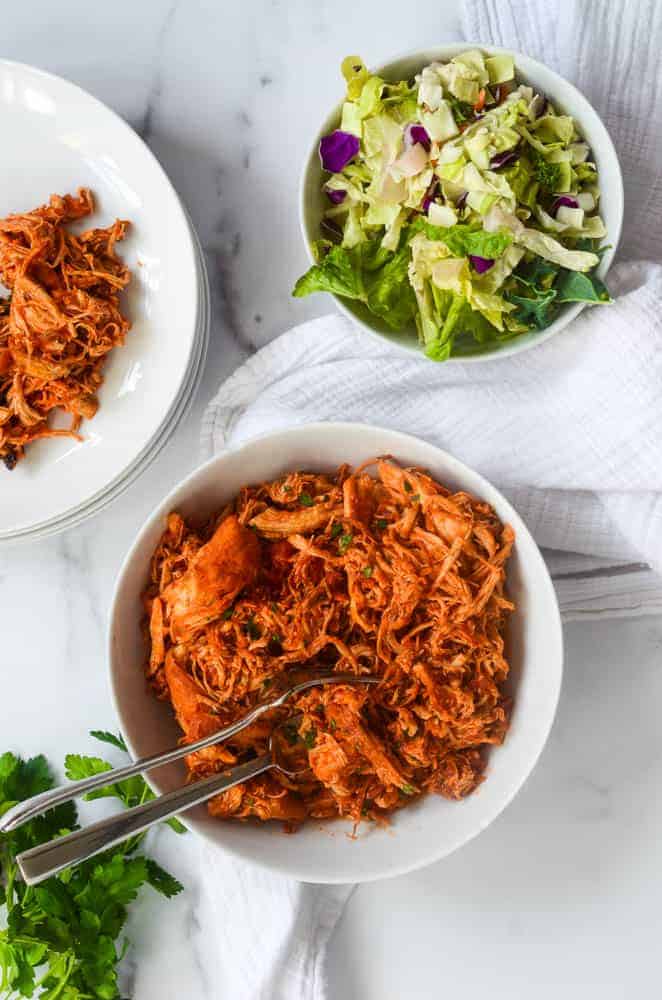 large white bowl of shredded chicken against marble backdrop.