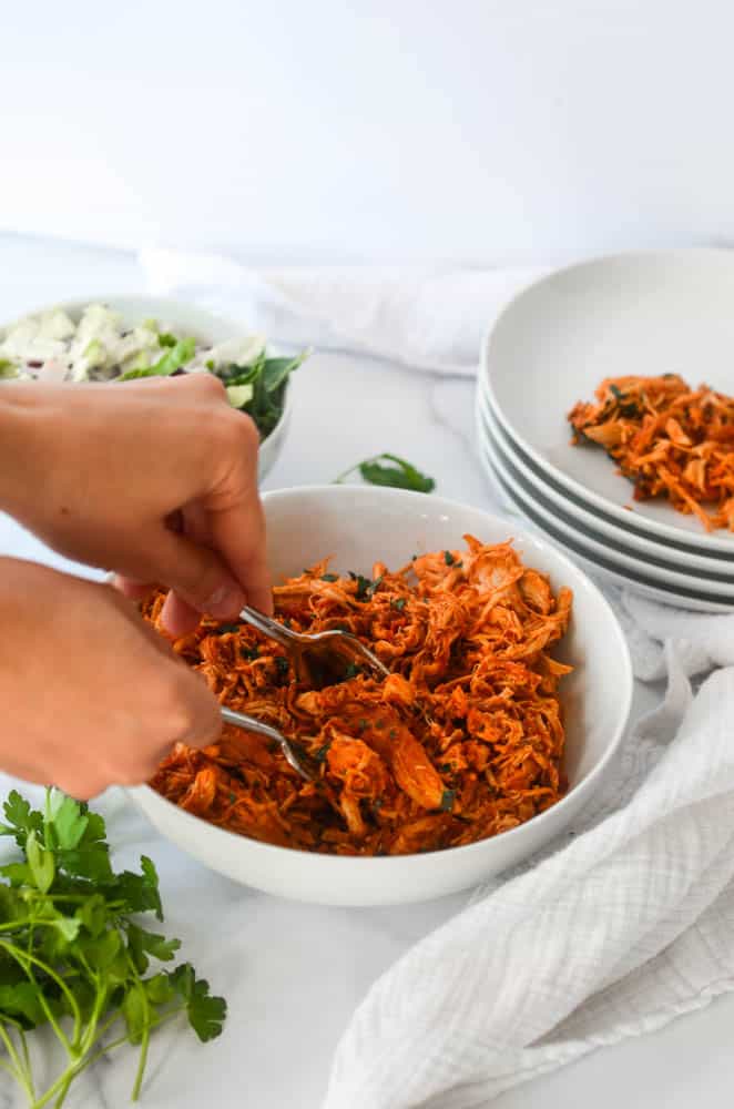 two hands shredding chicken with two forks. 