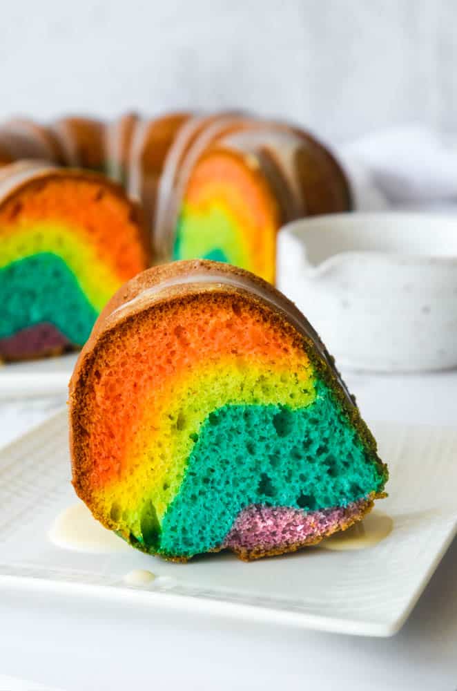 close up picture of one slice of rainbow bundt cake on white plate. 