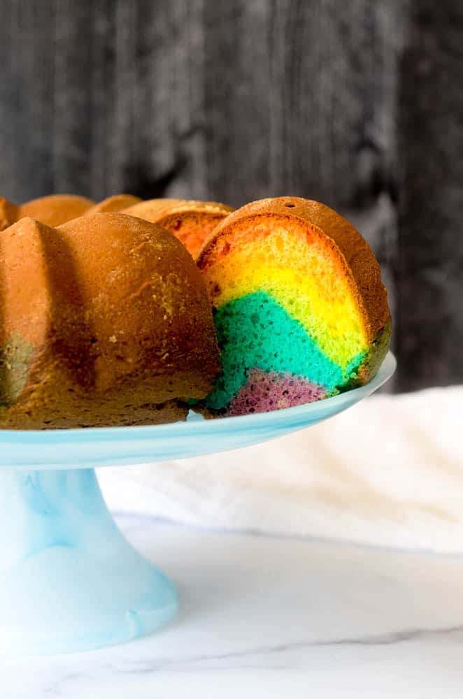 side view of bundt cake with one slice poking out to expose the rainbow colors. 