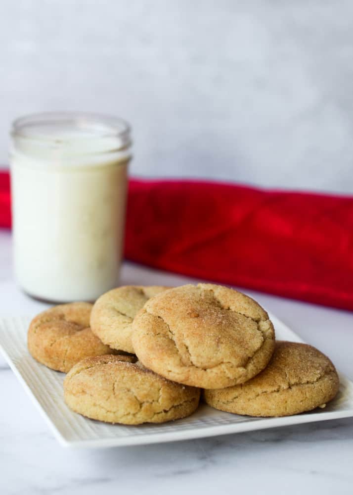 side picture of a plate of snickerdoodles with a glass of milk in the background with a red napkin. 