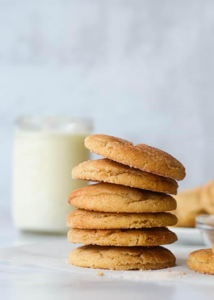 up close side picture of a stack of 6 snickerdoodles with a jar of milk in the background and other cookies. 