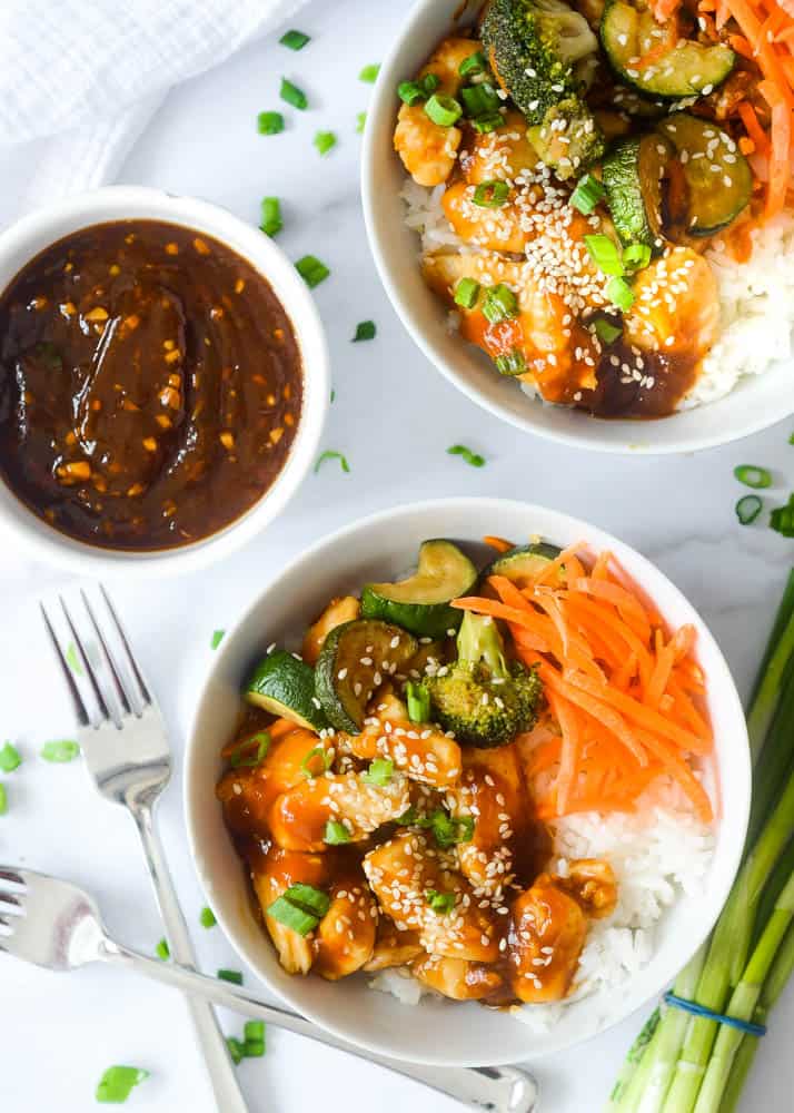 two teriyaki bowls in white ceramic with one white bowl of teriyaki sauce. 