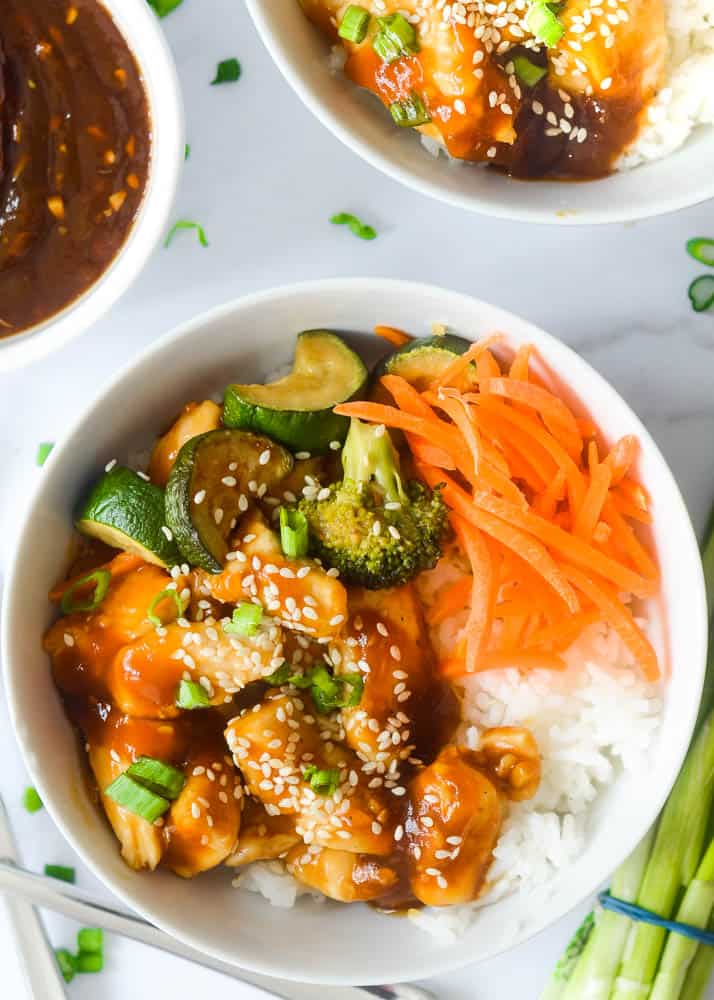 up close aerial picture of chicken teriyaki bowl with chicken, vegetables, carrots, and rice topped with sesame seeds and scallions. 