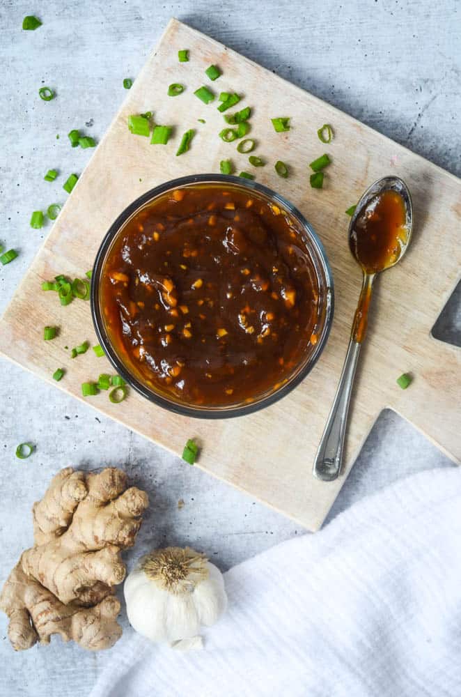 up close picture of a bowl of teriyaki sauce with messy spoon next to bowl on cutting board.