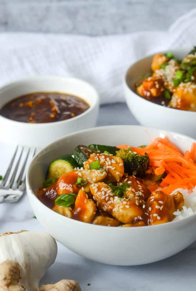 side show of chicken teriyaki bowl next to fork with two other white bowls in the background. 