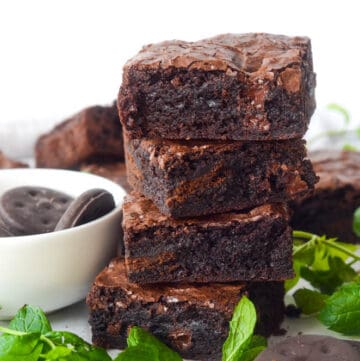 stack of 4 large thin mint brownies with bowl of thin mint cookies and mint in the background.