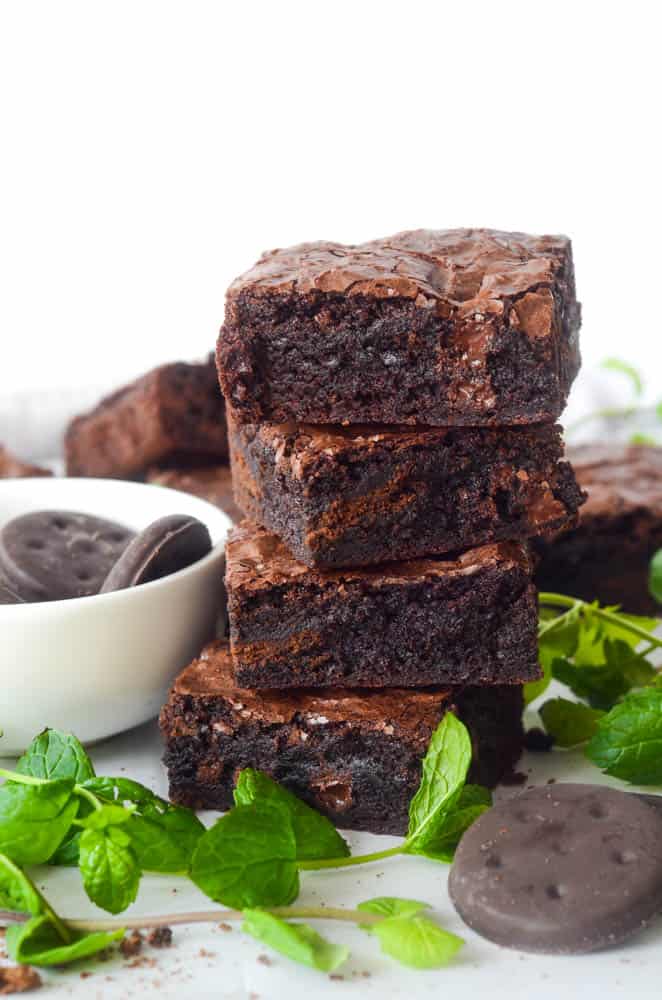 stack of 4 large thin mint brownies with bowl of thin mint cookies and mint in the background.