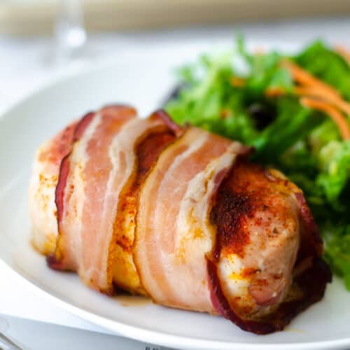 bacon wrapped pork chop on white plate with green salad.