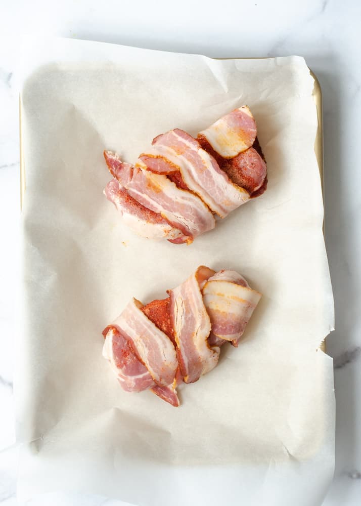 two pork chops wrapped in bacon on parchment paper. 