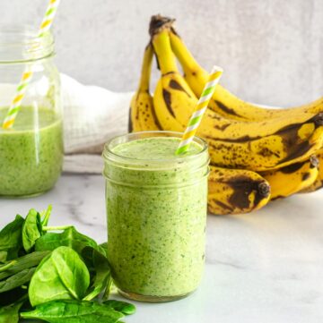 banana spinach smoothie in mason jar with loose spinach and bananas in background.