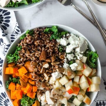 large white bowl full of kale, sweet potatoes, goat cheese, applies, wild rice, and almonds.
