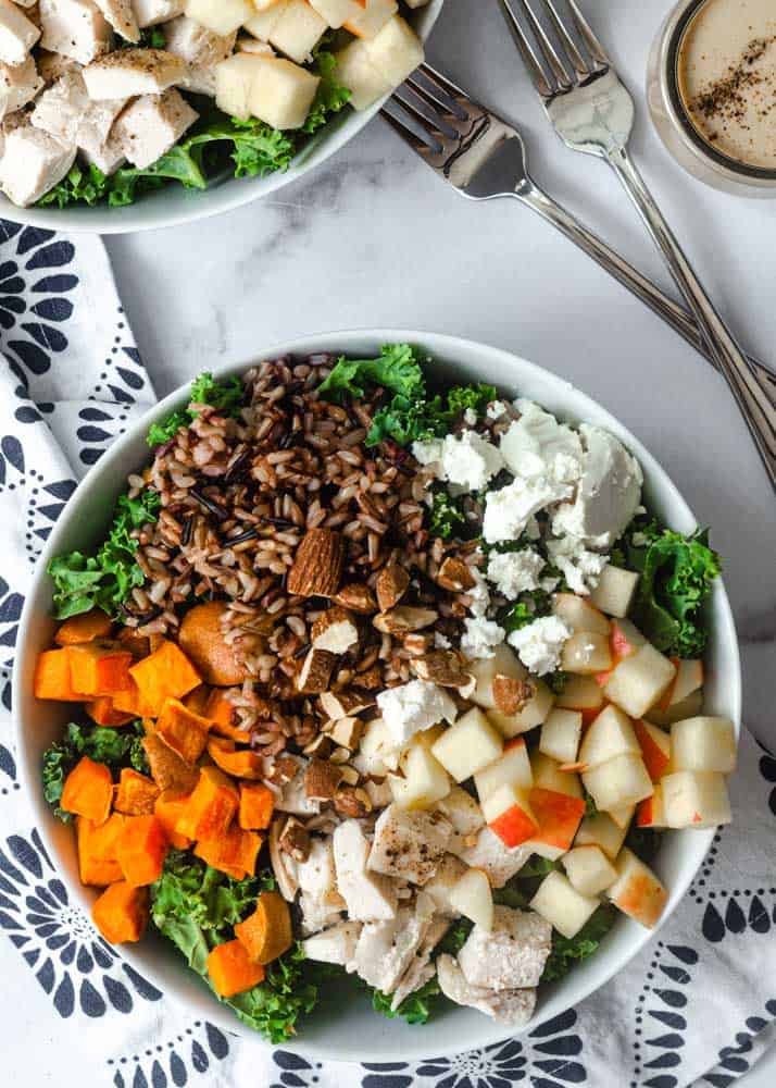 large white bowl full of kale, sweet potatoes, goat cheese, applies, wild rice, and almonds.