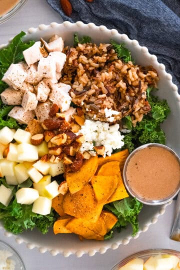 sweetgreen harvest bowl in a white scalloped bowl with sweet potatoes, apples, chicken, wild rice, almonds, and goat cheese over a bed of kale.