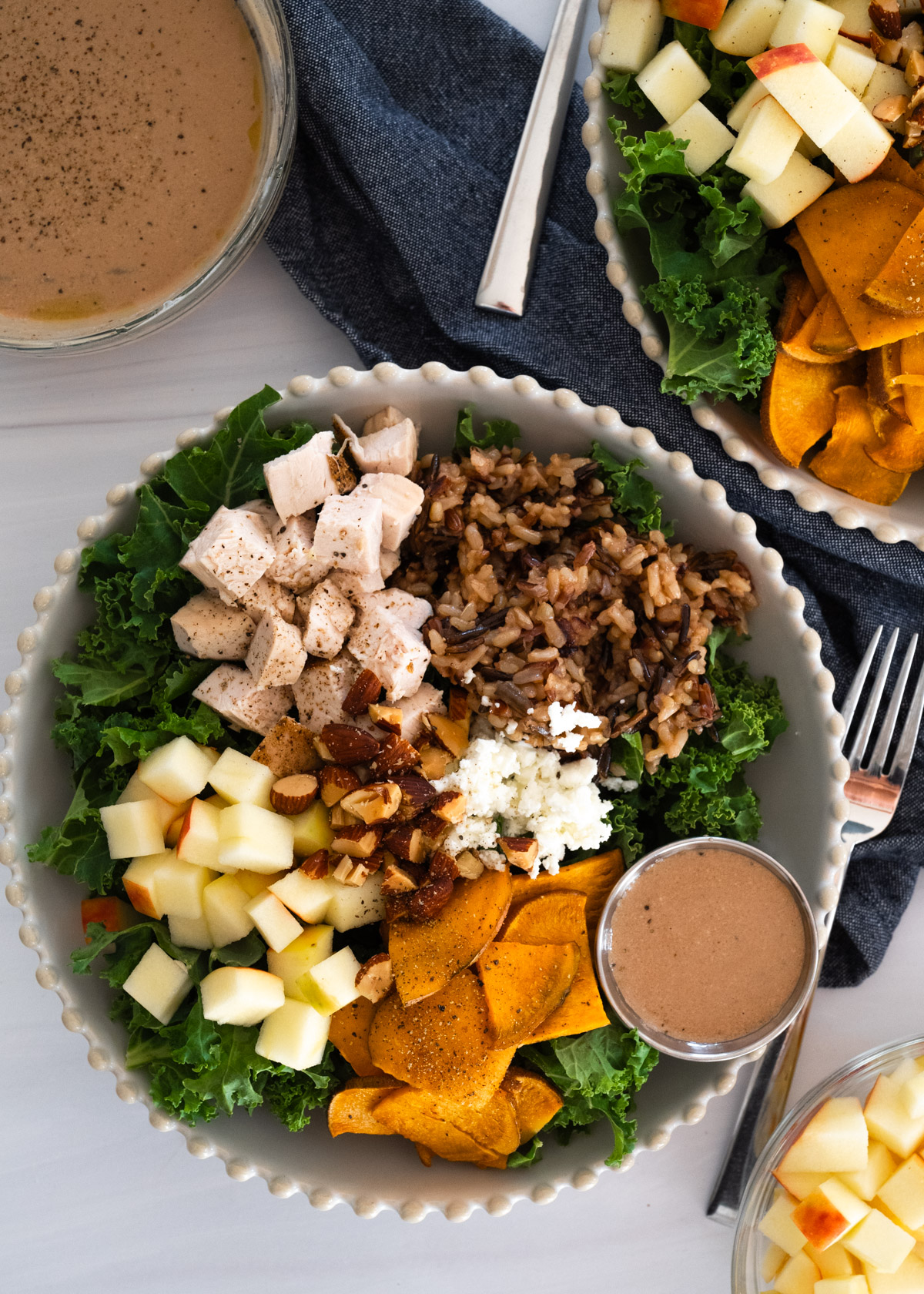 Aerial picture of two bowls of salad in white scalloped bowls with a side of dressing.