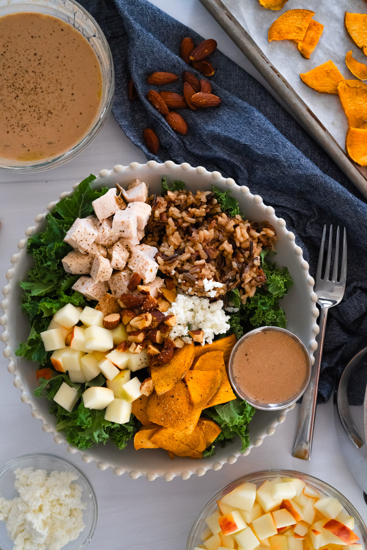Sweetgreen Harvest Bowl salad in a white bowl with smaller ingredient bowls strawn around the marble table. 