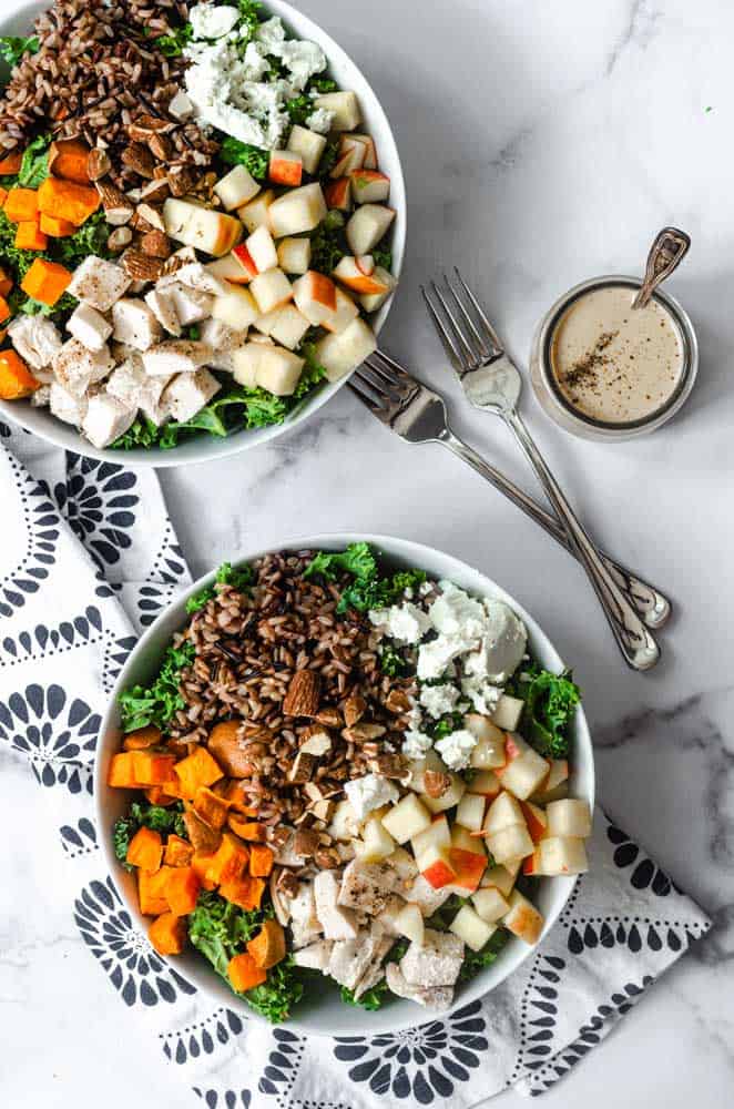 aerial photo of two large bowls of salad and jar of balsamic vinaigrette on white marble background. 