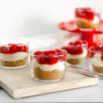 glass cup with cherry cheesecake on wooden board with several other glasses n background.