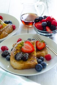 sourdough french toast with fresh berries and maple syrup on top on white plate.