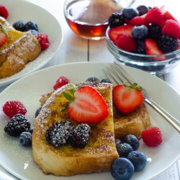 sourdough french toast with fresh berries and maple syrup on top on white plate.