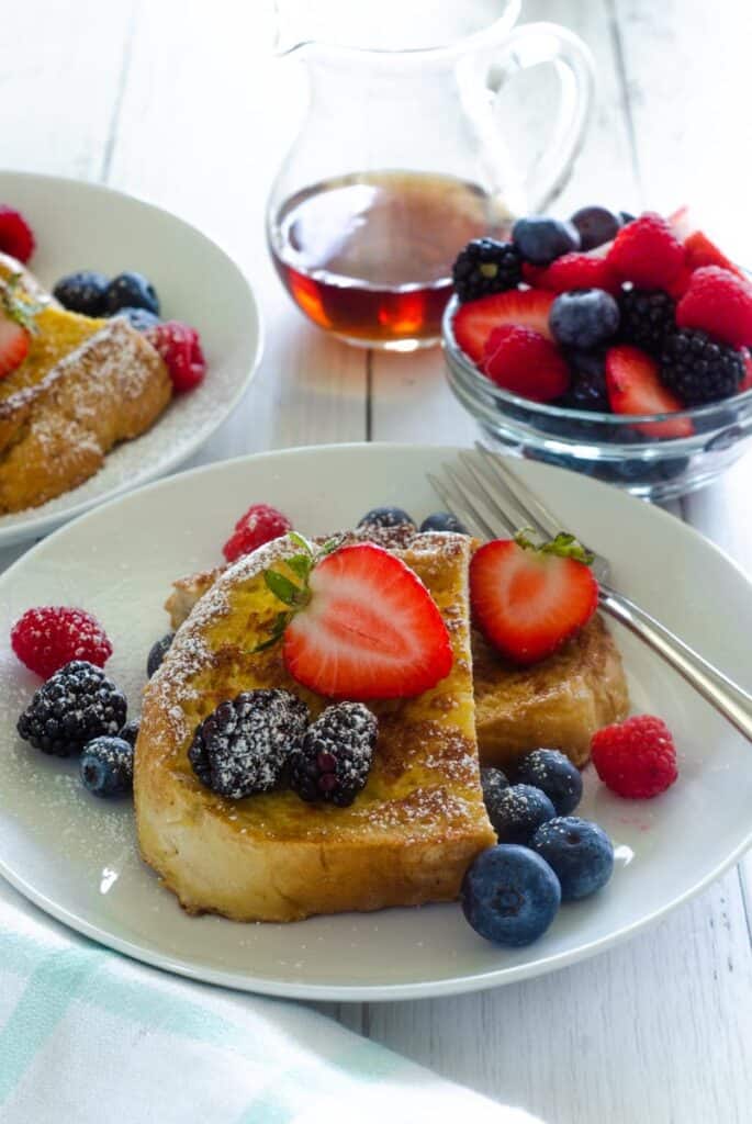 close up of french toast on white plate with fresh berries and confectionary sugar.