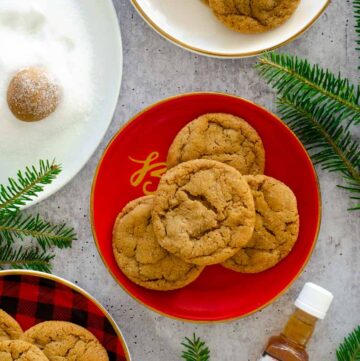 flat lay photo with 3 plates of bourbon ginger molasses cookies next to plate of sugar where dough ball is being rolled