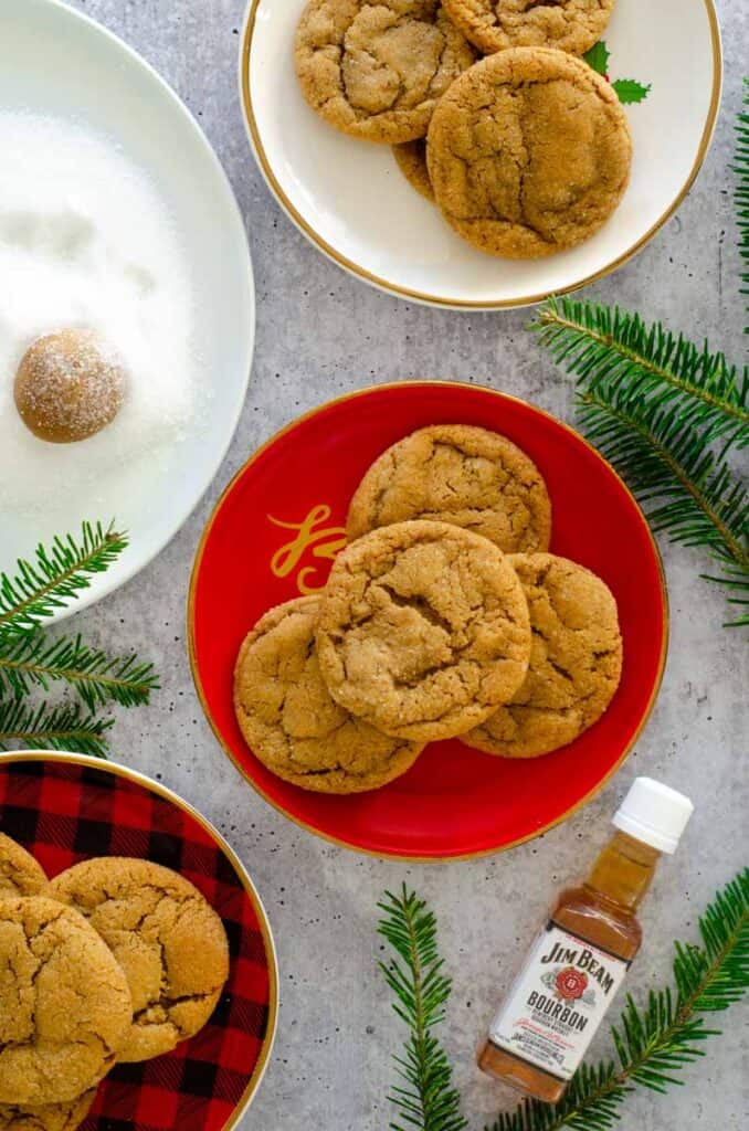 flat lay photo of three plates of cookies with tree sprigs and bottle of Jim Beam strewn about.