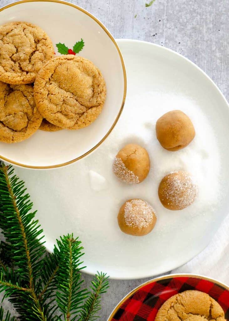 White plate with four balls of dough resting in granulated sugar with cookies on either side of the plate.