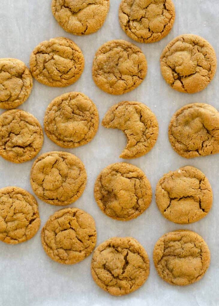 Aerial shot of several ginger molasses cookies on parchment paper with one cookie bitten into. 