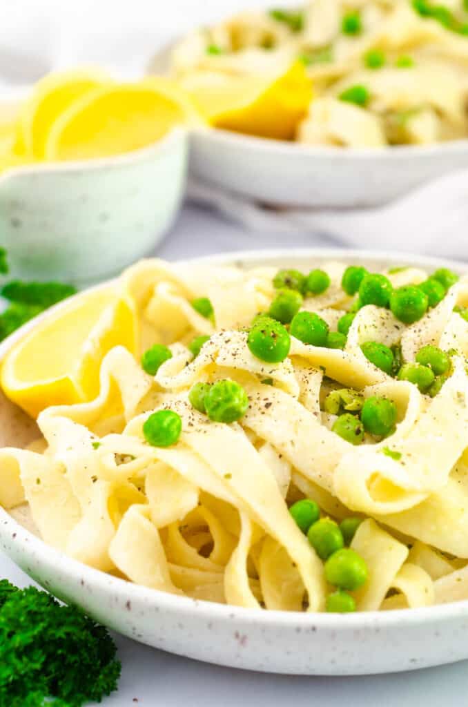 close up of pasta tossed with peas and black pepper on white plate. 