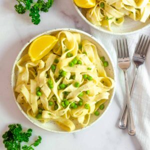 flatlay of large white plate with Boursin pasta, peas, and a lemon wedge. Parsley garnish around the plate along with two forks.