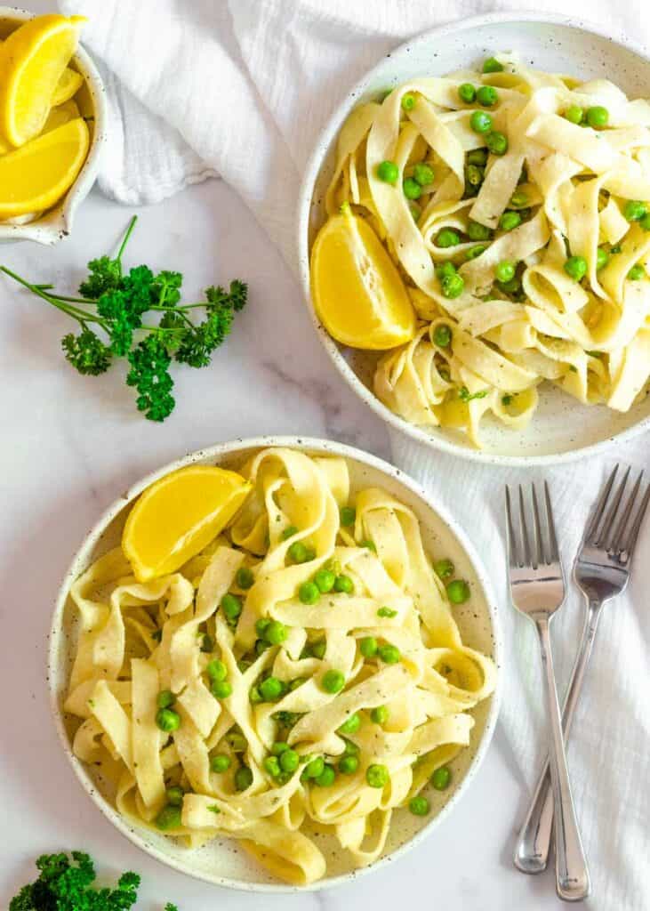 flatlay picture of two plates of pasta with large lemon wedge. 