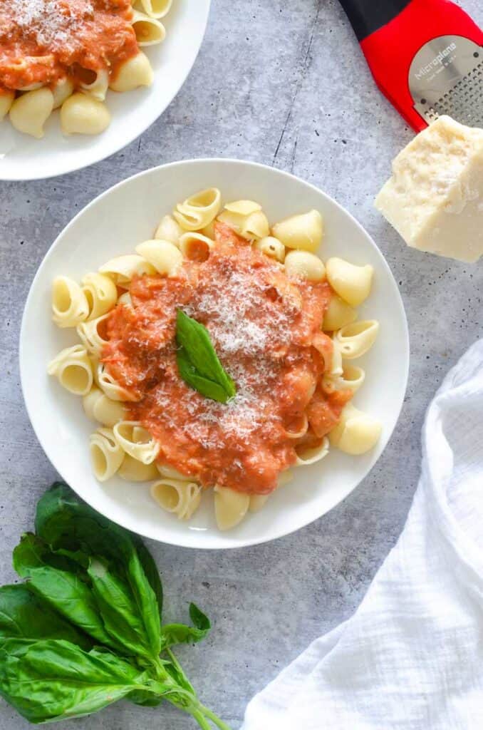 rose pasta on top of pasta on a white plate with basil and another pasta plate nearby. 