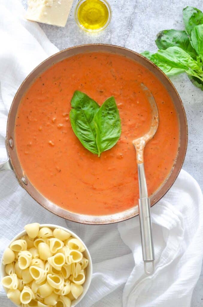 large sauce pan with pasta sauce and two large basil leaves with large serving spoon. 