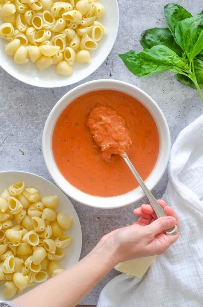 hand spooning a spoonful of rose pasta sauce out of white bowl. 