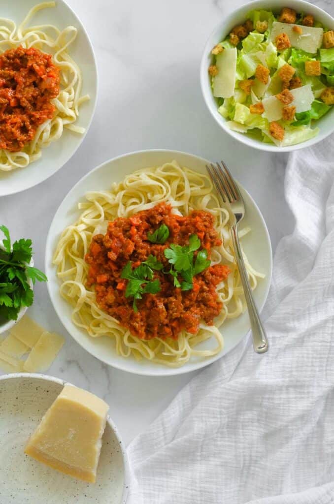 Large plate of linguine bolognese with parsley and parmesan surrounding the plate.