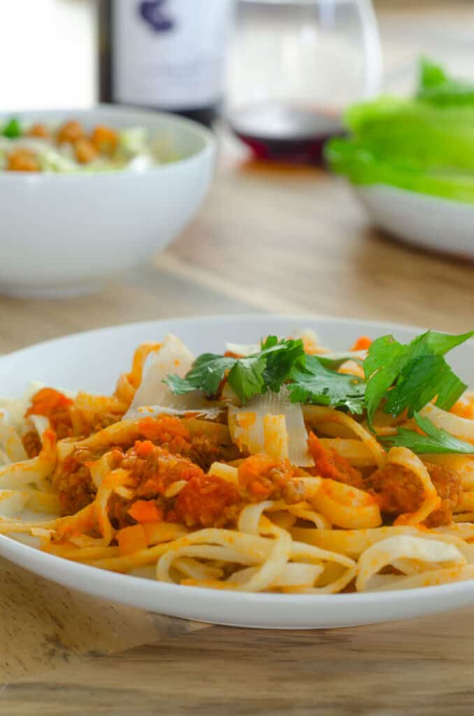 white plate with linguine and bolognese sauce mixed together with a generous helping of parsley on top. 