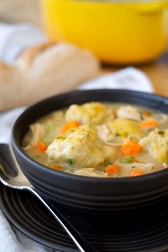 close up picture of a bowl of chicken and dumplings with a spoon next to the bowl. 