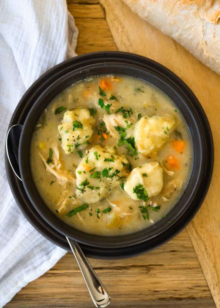 aerial picture of a brown bowl of chicken and dumplings garnished with fresh parsley. 