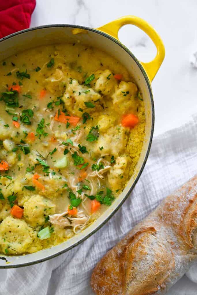 flatlay picture of chicken and dumplings in a dutch oven next to a fresh baguette. 