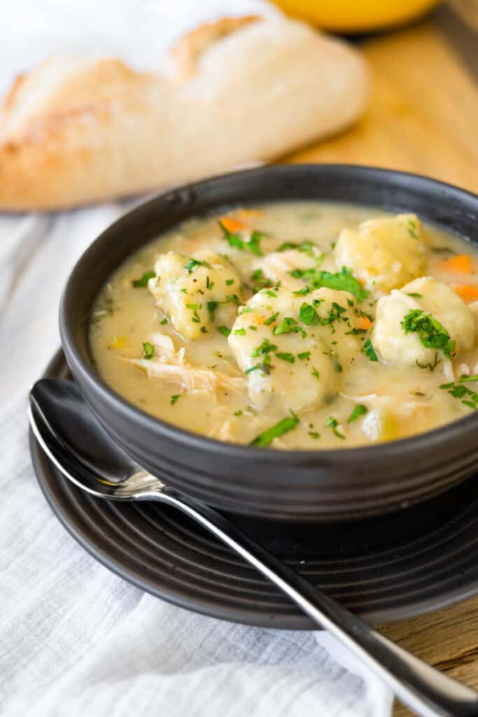 brown bowl of chicken and dumplings sprinkled with fresh parsley.