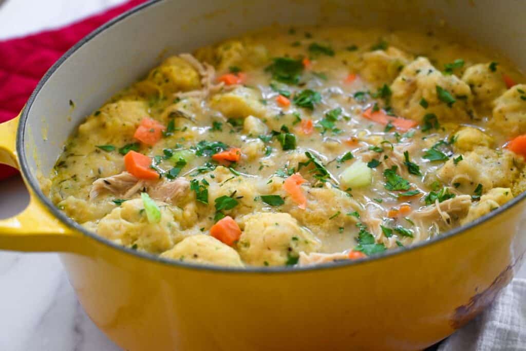 close up picture of chicken and dumplings in a large yellow dutch oven. 