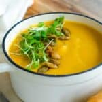 close up of a bowl of coconut pumpkin soup garnished with microgreens and pepitas.